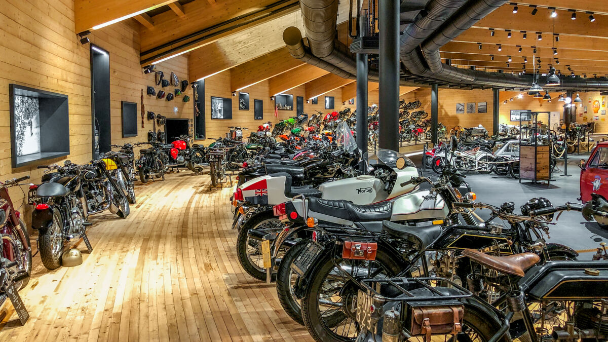 Halle aus hellem Holz mit Dutzenden historischen Motorrädern in Reihen, vorn eine Norton Halle aus hellem Holz mit Dutzenden historischen Motorrädern in Reihen, vorn eine Norton