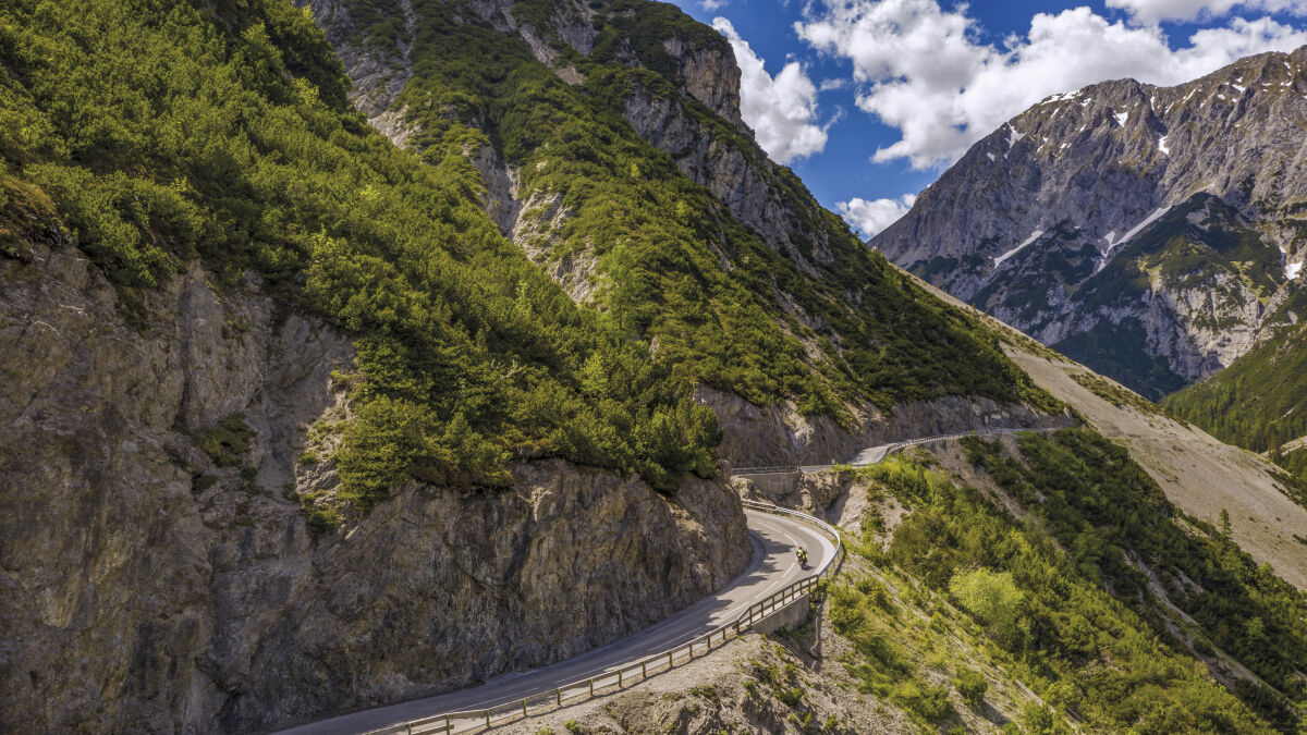 Zwei Motorräder in einer Kehre unter einer Felswand, gegenüber ein Kalkmassiv mit Schneeresten Zwei Motorräder in einer Kehre unter einer Felswand, gegenüber ein Kalkmassiv mit Schneeresten