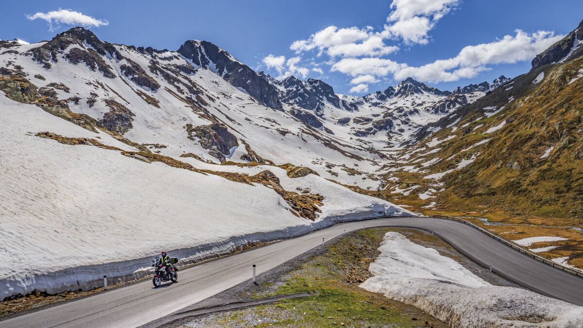 Motorrad auf einer Straße zwischen meterhohen Schneewänden, dahinter ein Talkessel mit Firnfeldern Motorrad auf einer Straße zwischen meterhohen Schneewänden, dahinter ein Talkessel mit Firnfeldern